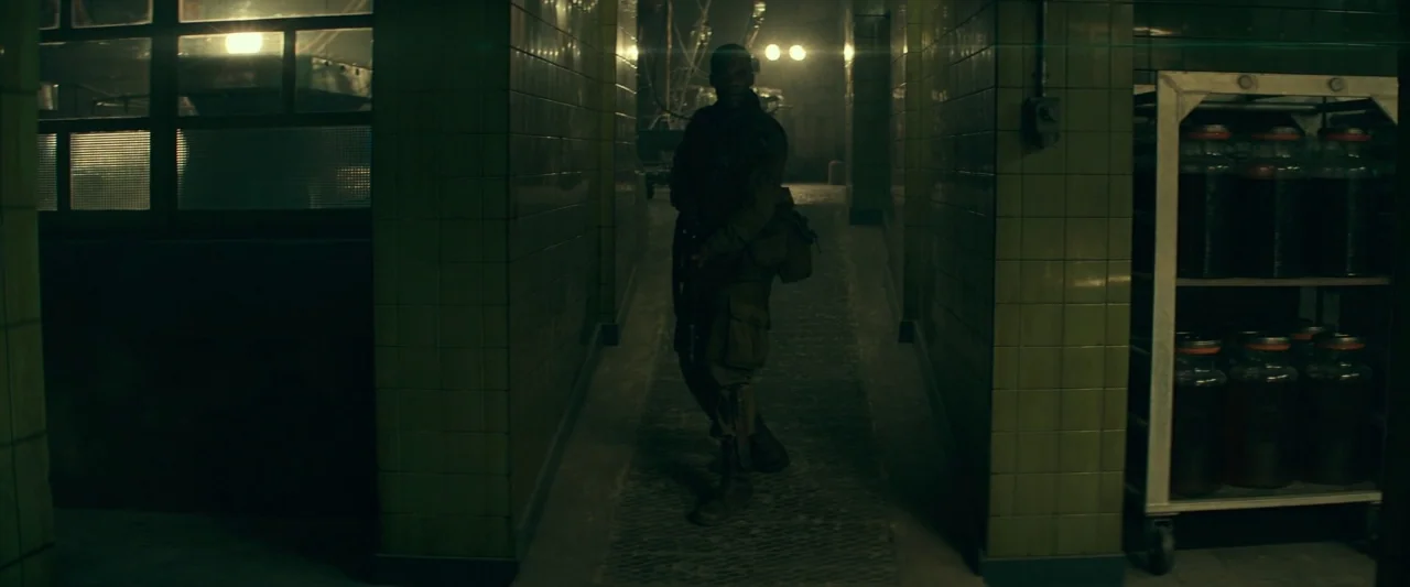 Overlord (2018) movie still: fullbody — A narrow dimly lit corridor features olive green tiled walls and shelving units.