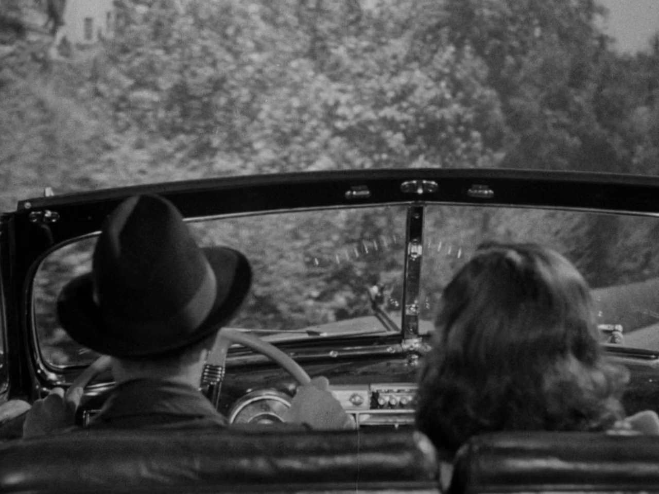 Phantom Lady (1944) movie still: medium — The front seat interior of a vintage automobile with a black leather dashboard. A man wearing a fedora…