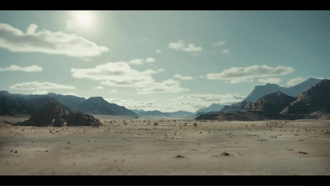 Lee Soo Man: King of K-Pop (2025) movie still: establishing — A vast, arid desert floor stretches towards jagged mountain ranges under a bright sky.…