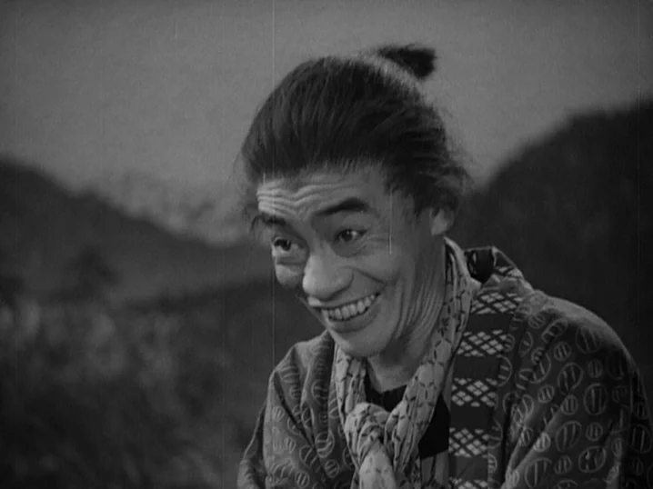 The Men Who Tread on the Tigers Tail (1945) movie still: closeup — A man stands outdoors in a mountainous region with blurred foliage in the…