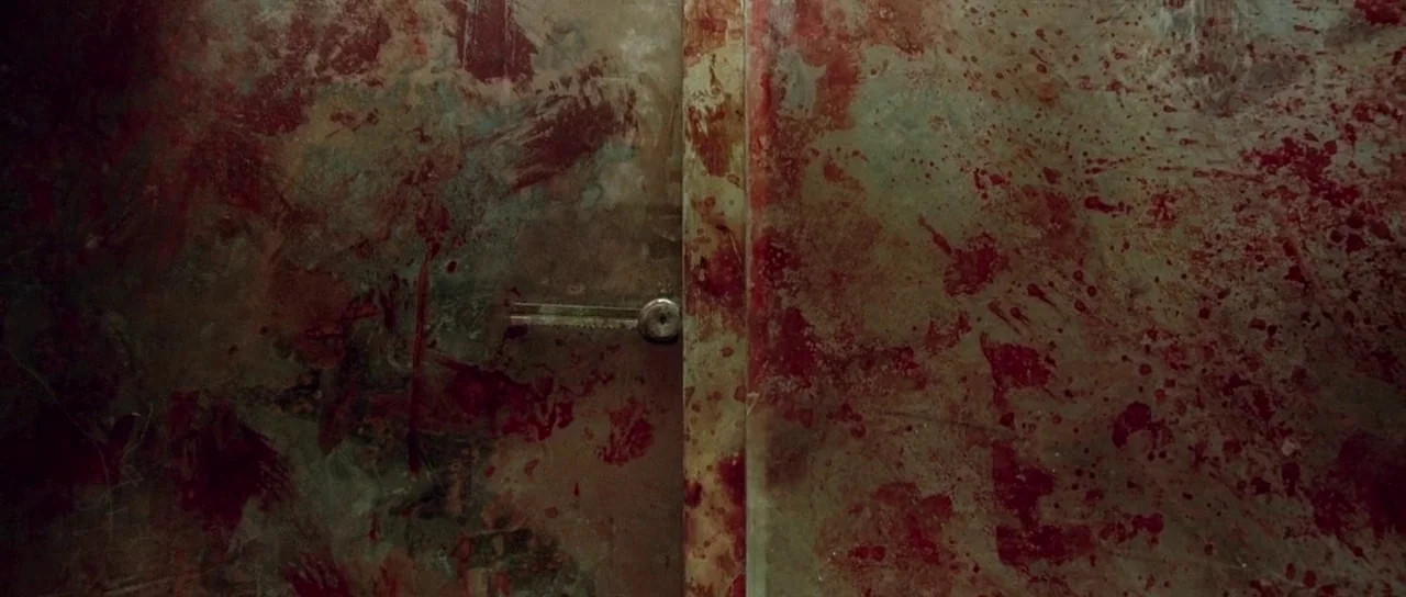 The Hills Have Eyes (2006) movie still: wide — A metal door sits between two walls covered in thick patterns of fresh blood. The surface of the…