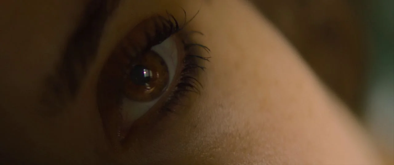 Palm Springs (2020) movie still: closeup — A extreme close-up of a human eye in a dark, dimly lit environment. The subject rests against a soft…