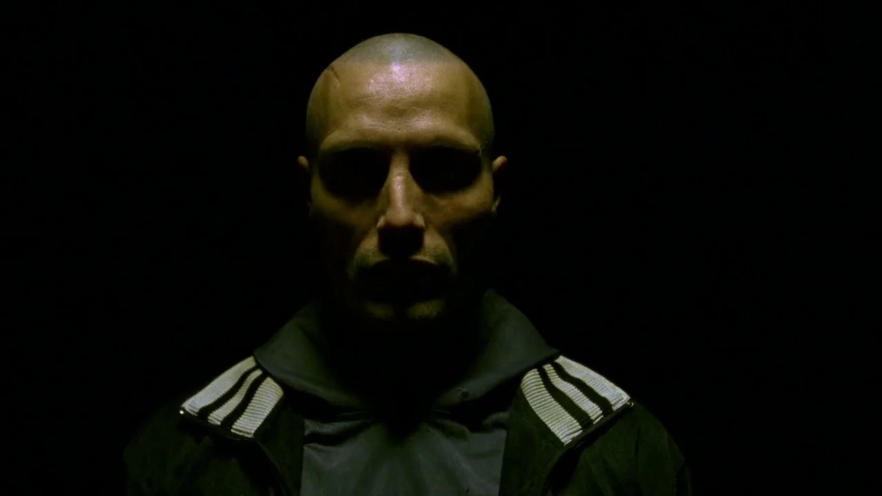 Pusher II (2004) movie still: closeup — A man stands against a pitch black backdrop with no visible environmental features. His head and shoulders…
