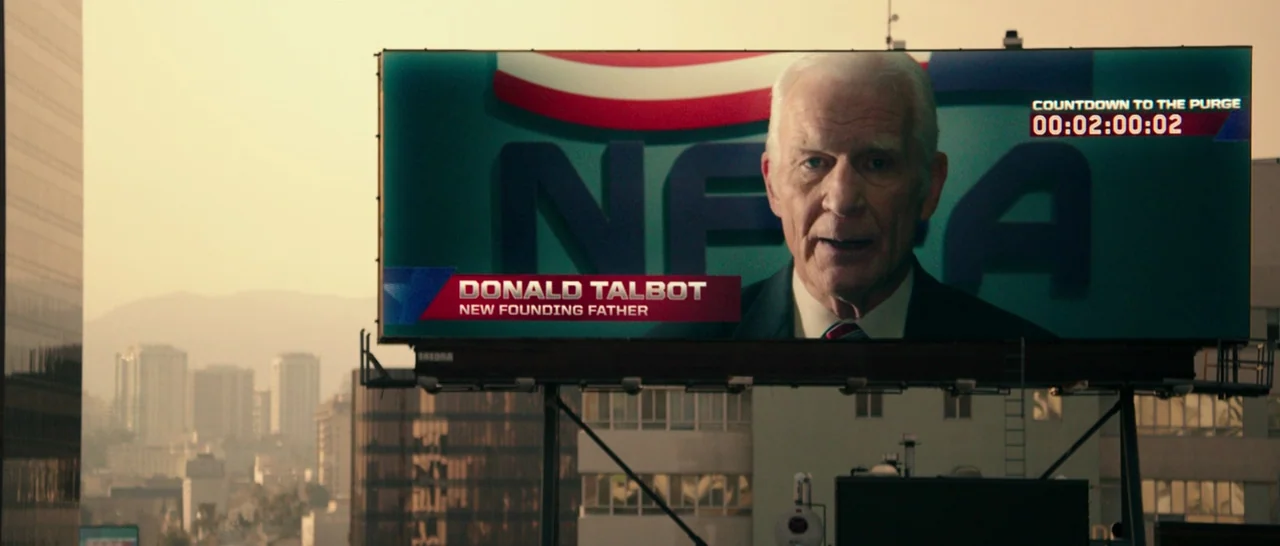 The Purge: Anarchy (2014) movie still: wide — An urban cityscape with a large billboard in the foreground displaying a political message. The…