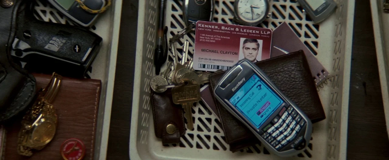 Michael Clayton (2007) movie still: closeup — A plastic airport security tray contains personal items including keys, a wallet, and a watch. An…