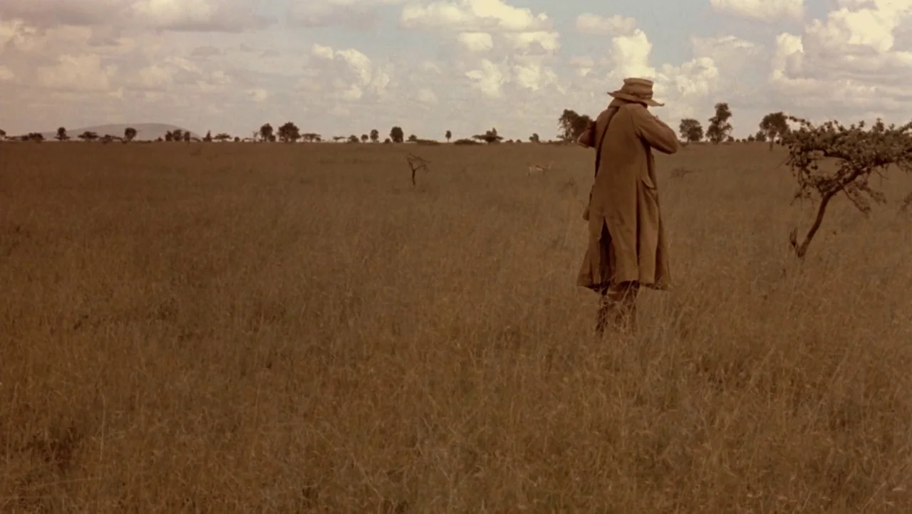 Mountains of the Moon (1990) movie still: wide — A vast, grassy plain extends to the horizon under a pale, partly cloudy sky. A solitary man in a…