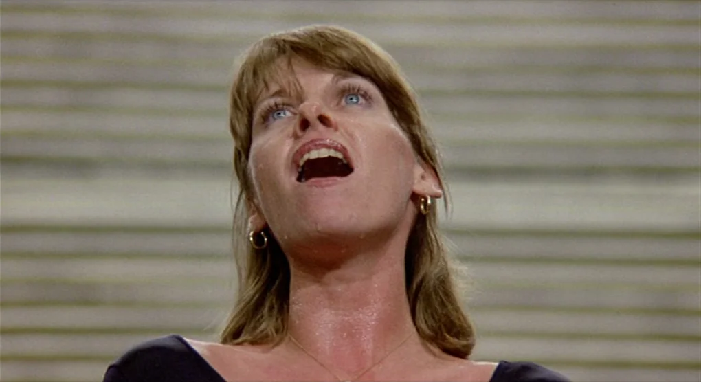 All That Jazz (1979) movie still: closeup — A woman stands before a background of horizontal light-colored steps or parallel lines. She tilts her…