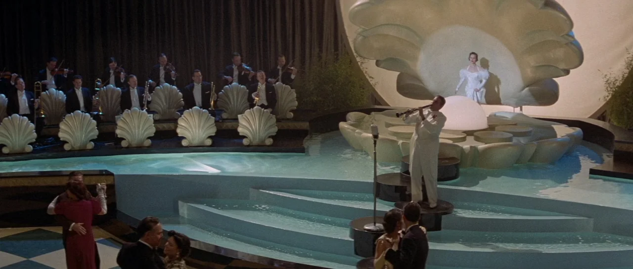 The Rocketeer (1991) movie still: wide — A lavish ballroom features a large shell-shaped stage set above a pool of light blue water. A clarinetist…