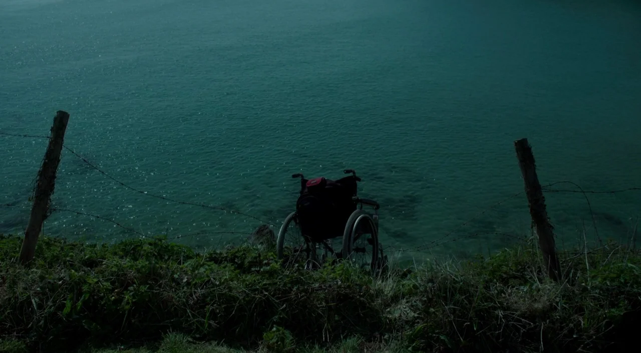 Miss Peregrine’s Home for Peculiar Children (2016) movie still: wide — A dark, empty wheelchair sits on a grassy cliff edge overlooking deep blue…
