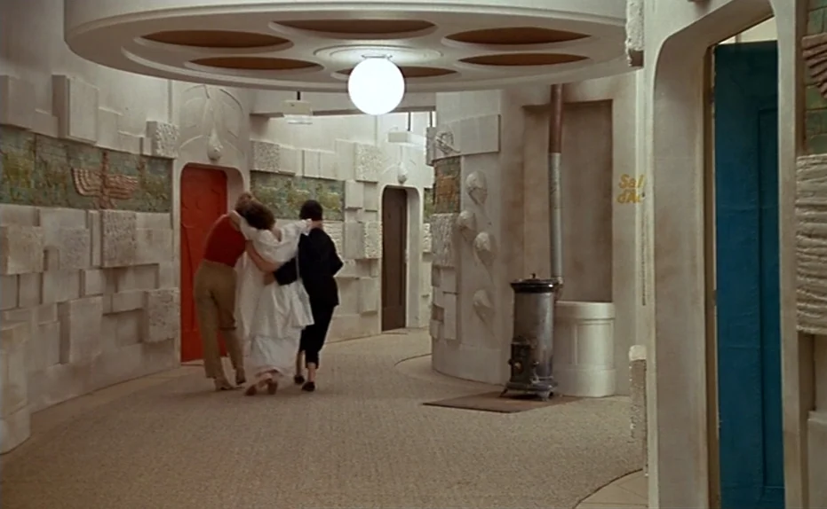 Life Is A Bed of Roses (1983) movie still: fullbody — An interior hallway features white textured walls adorned with low-relief geometric and…