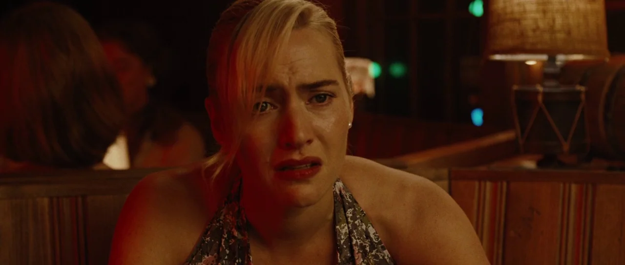 Revolutionary Road (2008) movie still: closeup — A dimly lit restaurant booth at night features striped wooden backrests and warm lamp light. A…