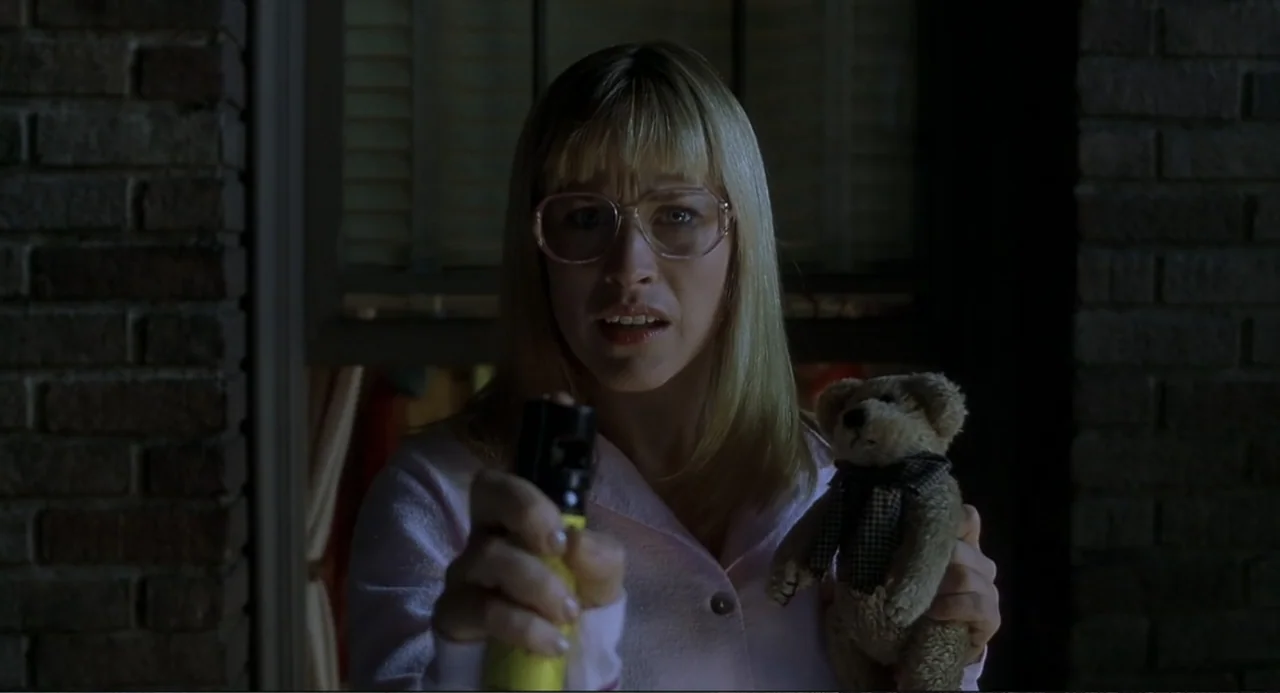 Little Nicky (2000) movie still: medium — A woman stands in a dark doorway framed by a brick wall and a window. She holds a small teddy bear in one…