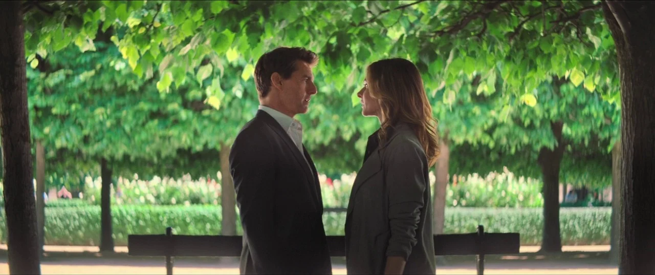 Mission: Impossible – Fallout (2018) movie still: medium — A tree-lined walkway in a park features a wooden bench placed centrally. A man and woman…