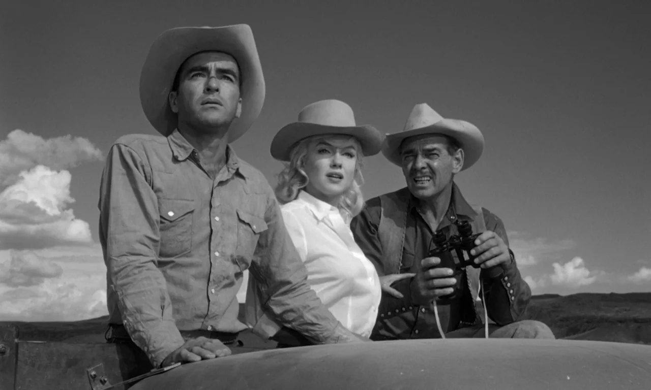 The Misfits (1961) movie still: medium — Three people in cowboy hats observe a distant horizon in an open desert landscape. They stand together in…