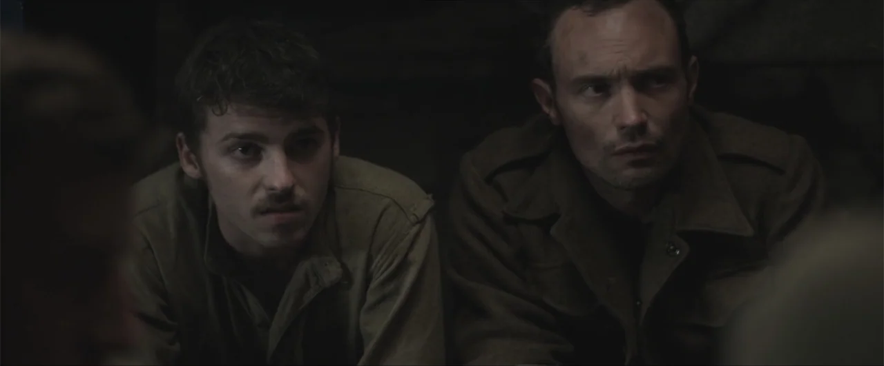 Behind the Line: Escape to Dunkirk (2020) movie still: medium — A cramped, dimly lit earthen shelter reinforced with dark shadows and indistinct…