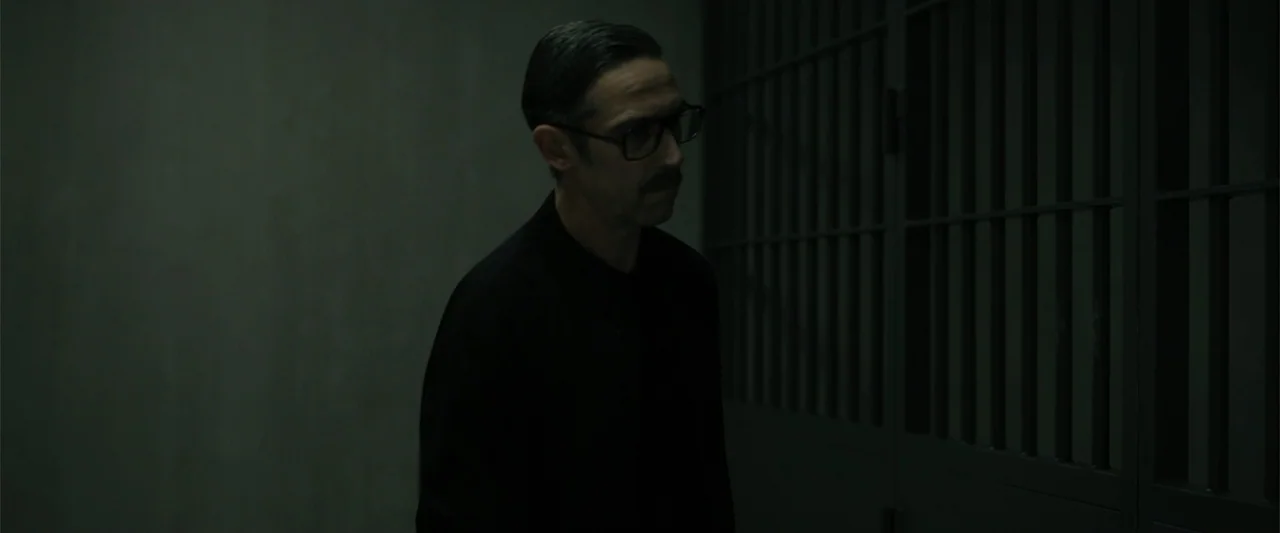 Den of Thieves 2: Pantera (2025) movie still: medium — A dark space with a heavy metal gate and smooth walls. A man in a dark shirt stands near the…