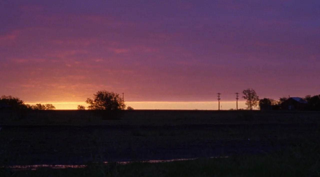 Boys Don’t Cry (1999) movie still: establishing — A flat field sits under a vast, dark purple sky at sunset. A thin, bright orange line glows…
