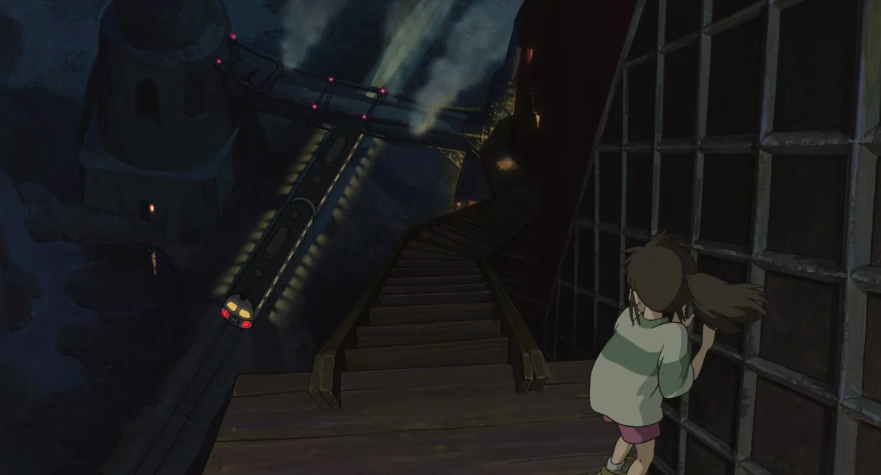 Spirited Away (2001) movie still: wide — A dark, elevated outdoor wooden staircase overlooks a landscape at night. A train moves along tracks while…