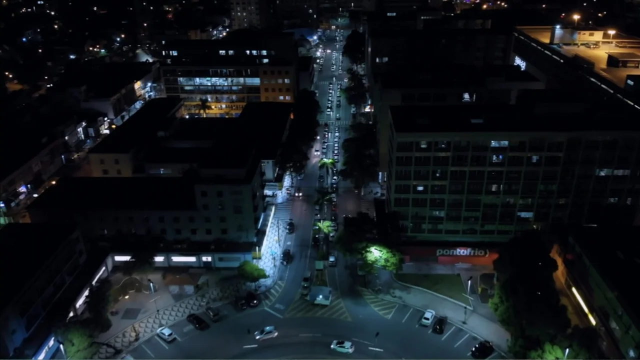 The Grotto (2022) movie still: establishing — An aerial view of a nighttime urban environment shows multi-story buildings surrounding a central…