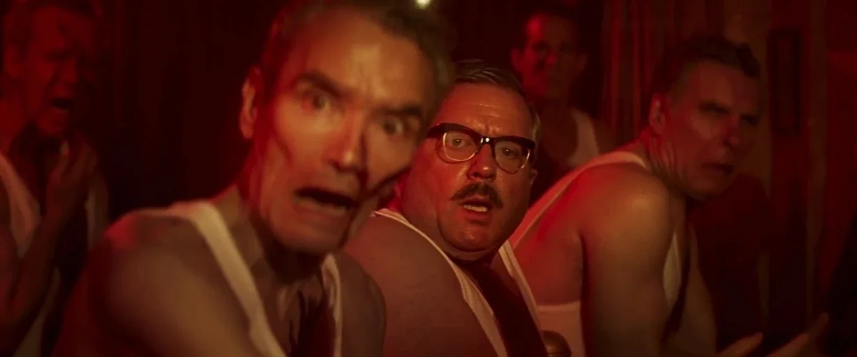 Last Night in Soho (2021) movie still: medium — A dimly lit room is illuminated by a deep red, artificial light source. Four men wearing white…
