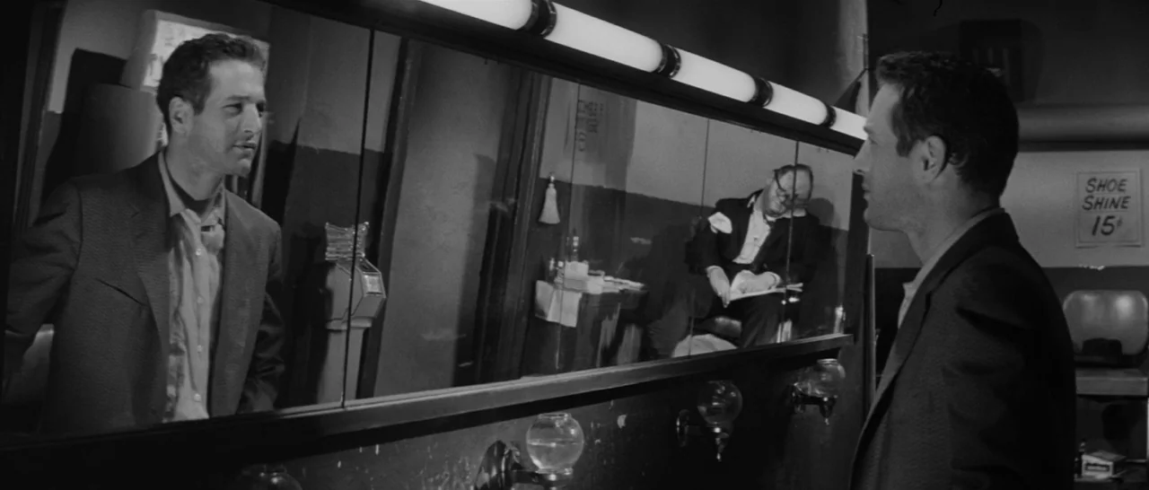 The Hustler (1961) movie still: medium — A dimly lit room features a long wall mirror reflecting a man seated nearby. The man in the foreground…