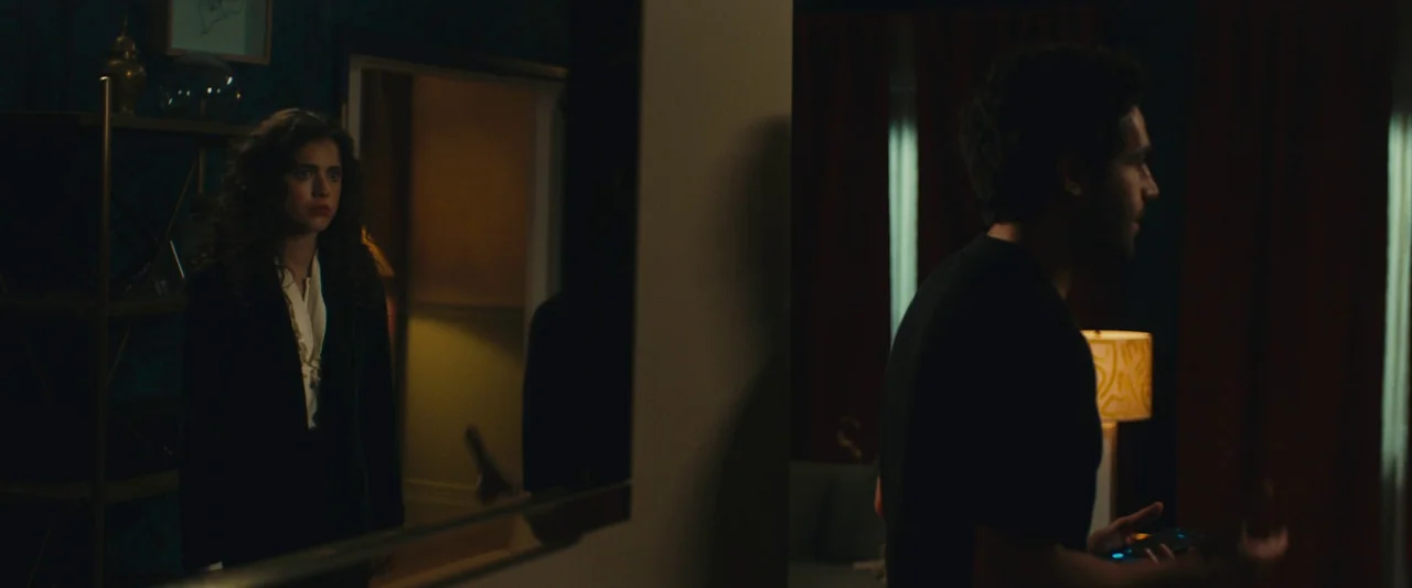 Sanctuary (2023) movie still: medium — A dimly lit apartment features dark blue walls and patterned curtains in the background. A man stands in the…