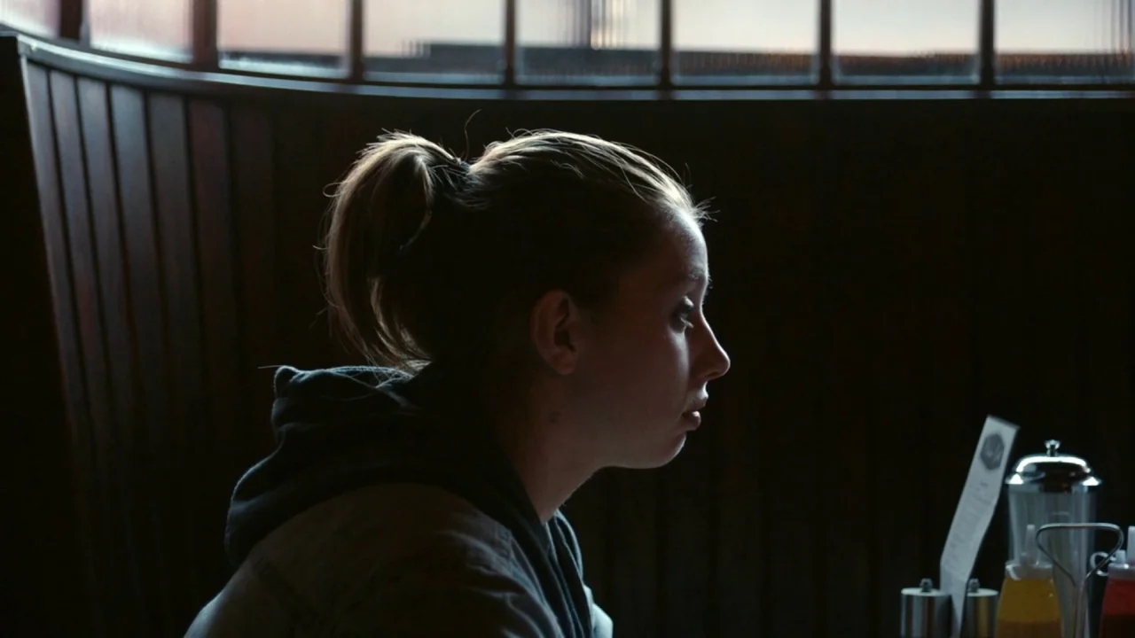 A Date for Mad Mary (2016) movie still: medium — A dark restaurant booth features dark wooden paneling and a window with horizontal muntins. A young…