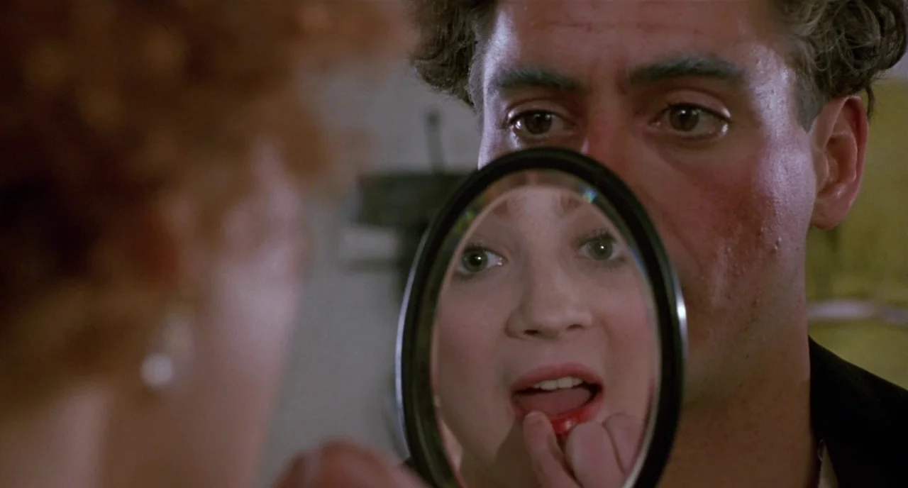 Chaplin (1992) movie still: closeup — A man and woman are in a dimly lit indoor space close together. The woman looks into a small handheld mirror…