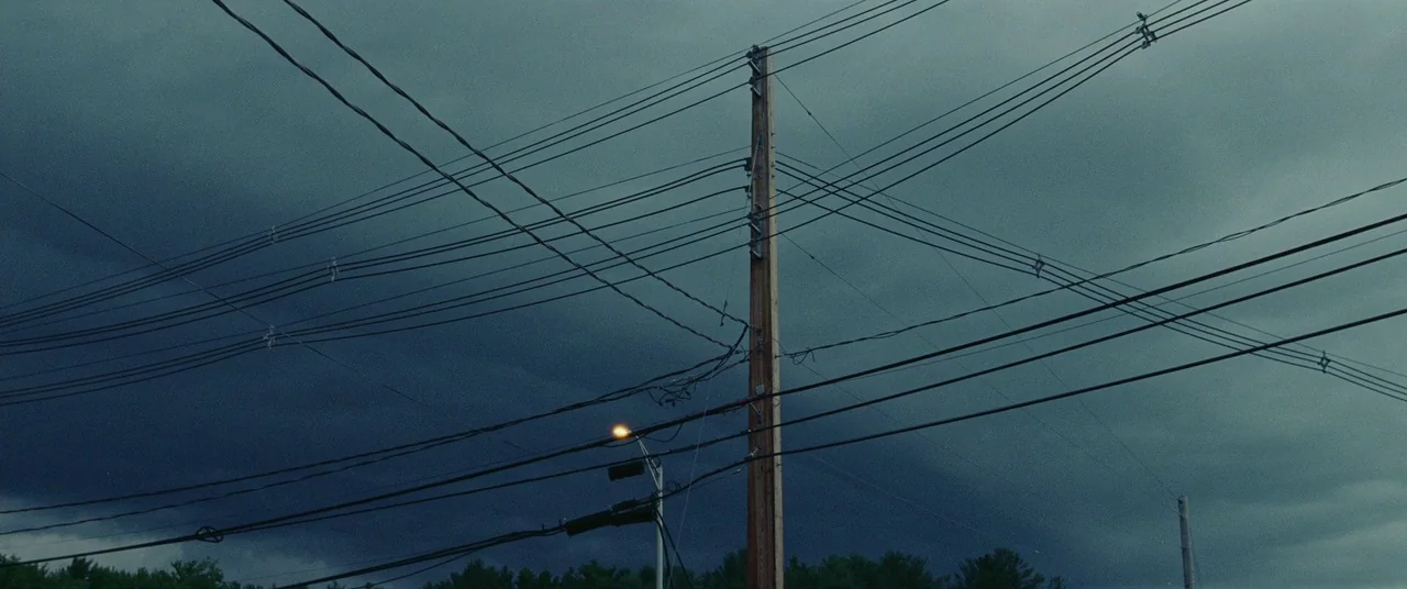 Sound of Metal (2019) movie still: establishing — A wooden utility pole stands center frame against a dense, dark, overcast storm sky. Numerous…