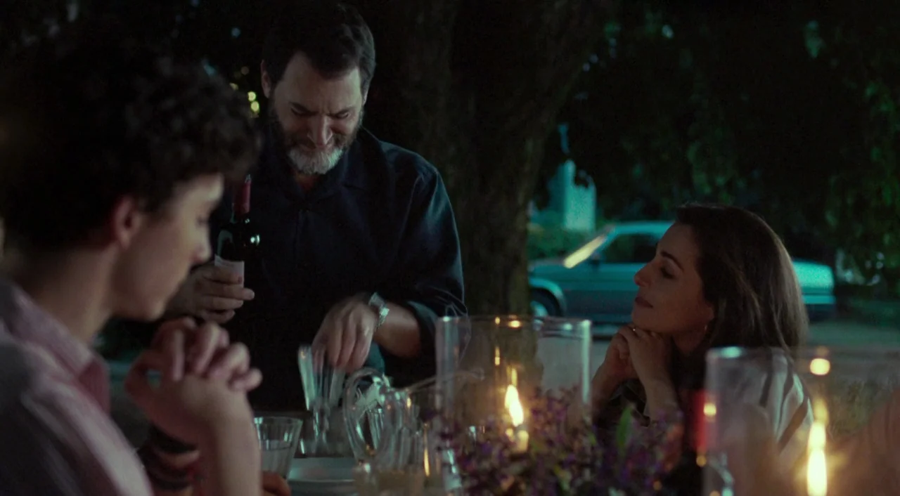 Call Me By Your Name (2017) movie still: medium — An outdoor evening dinner setting with a blurred car visible in the dark distance. A man pours…