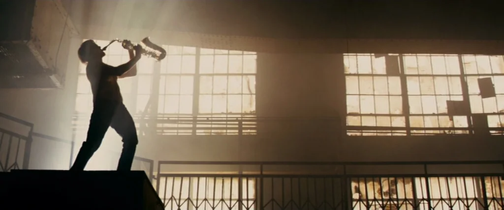 MacGruber (2010) movie still: wide — An industrial building interior features large multi-pane windows and metal railing balconies. A shirtless man…