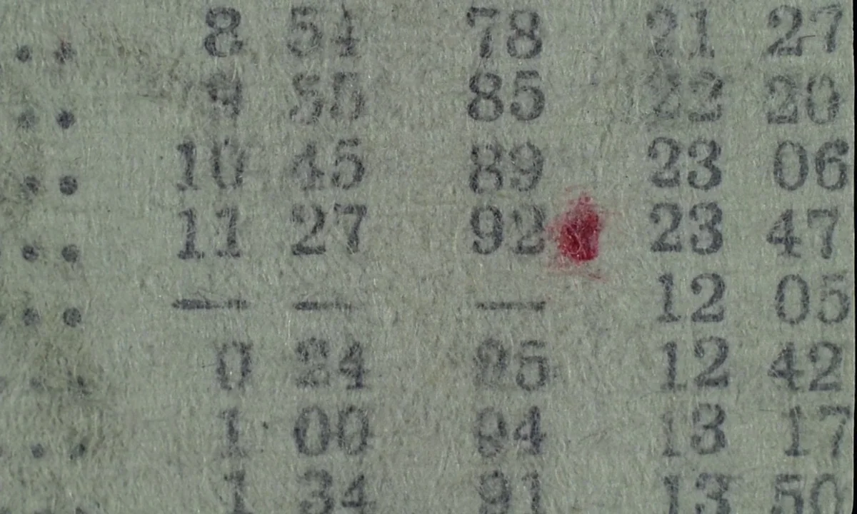 Immoral Tales (1974) movie still: closeup — A close-up view shows a piece of coarse, fibrous paper with rows of printed numbers. A small, irregular…
