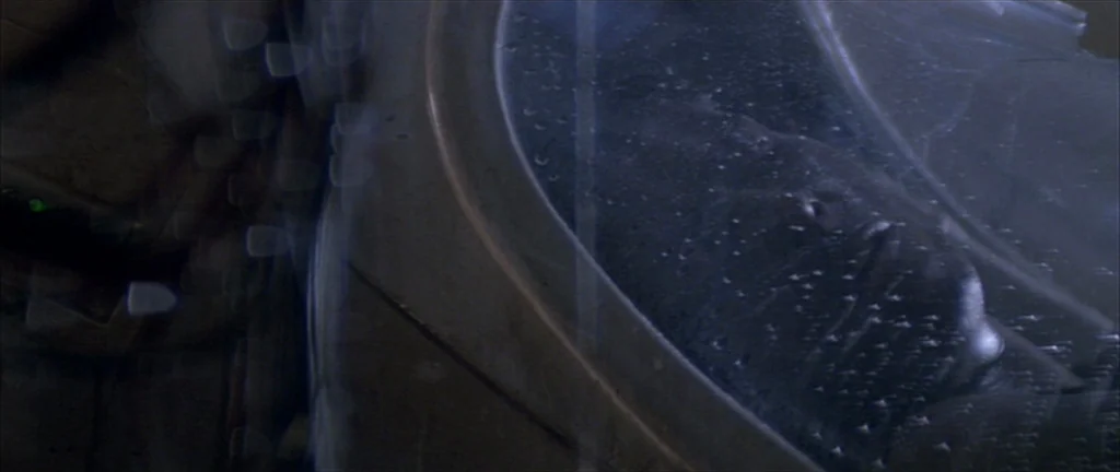 Alien 3 (1992) movie still: closeup — A person lies inside a translucent circular chamber covered in condensation droplets. The dark figure is…