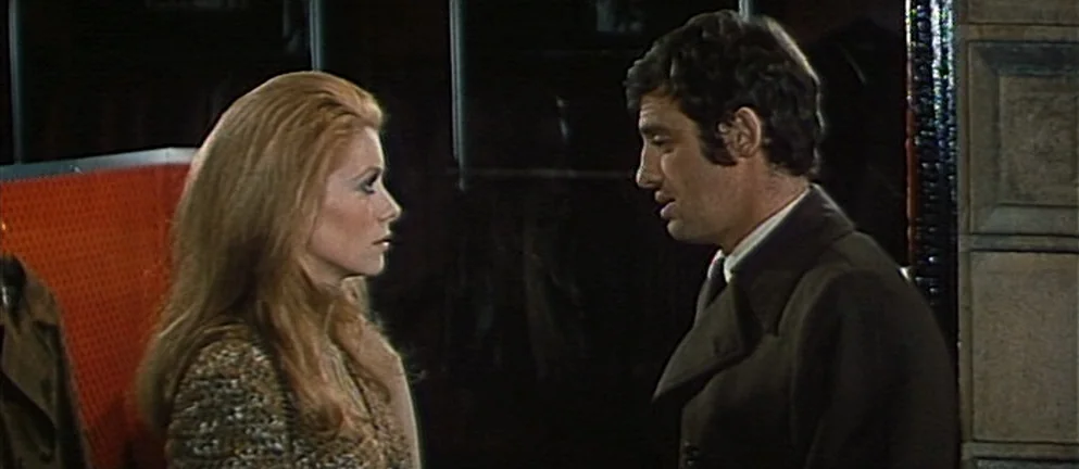 Mississippi Mermaid (1969) movie still: medium — A dimly lit cloakroom features a dark wall and a bright orange textured panel. A man and woman…