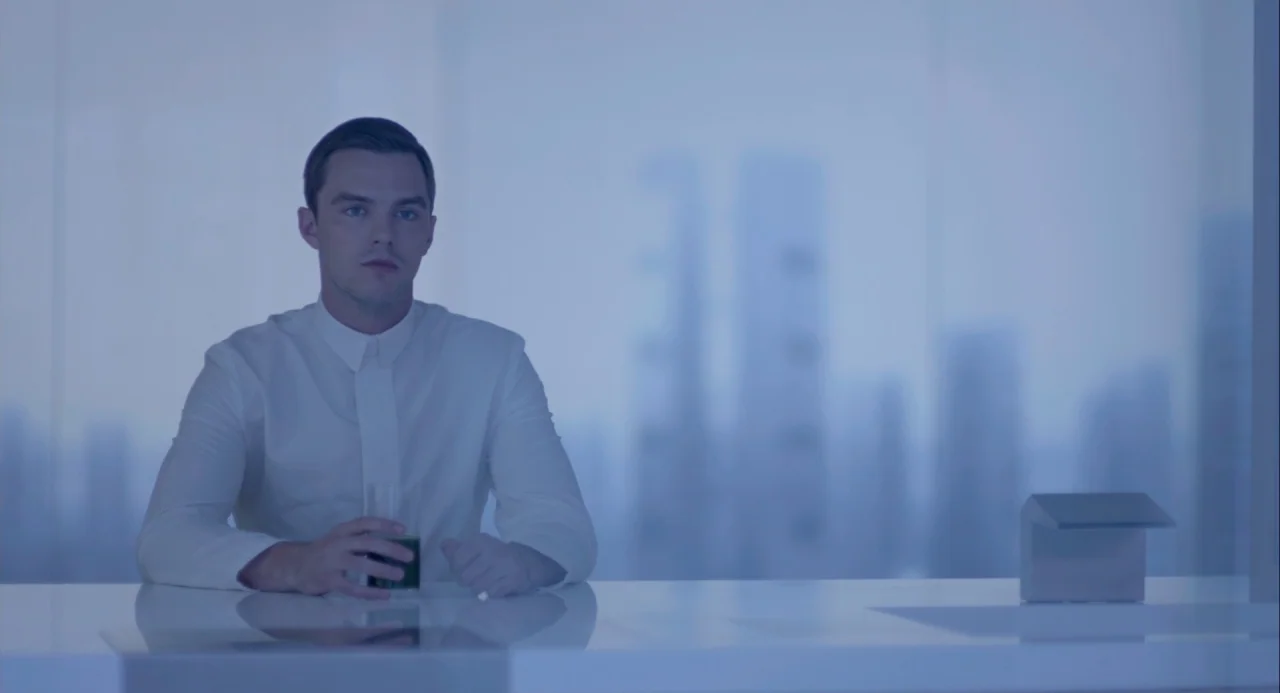 Equals (2015) movie still: medium — A minimalist white room overlooks a blurred cityscape through a large glass wall. A man sits at a white surface…