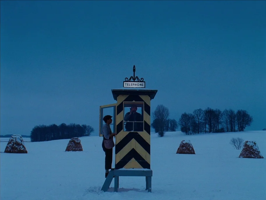 The Grand Budapest Hotel (2014) movie still: wide — A remote, black-and-yellow striped telephone booth stands in the middle of a vast, snowy…