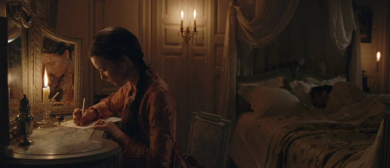 Madame Bovary movie still: medium — A dimly lit 19th-century room features a woman at a vanity and a canopy bed. The woman writes a letter by…