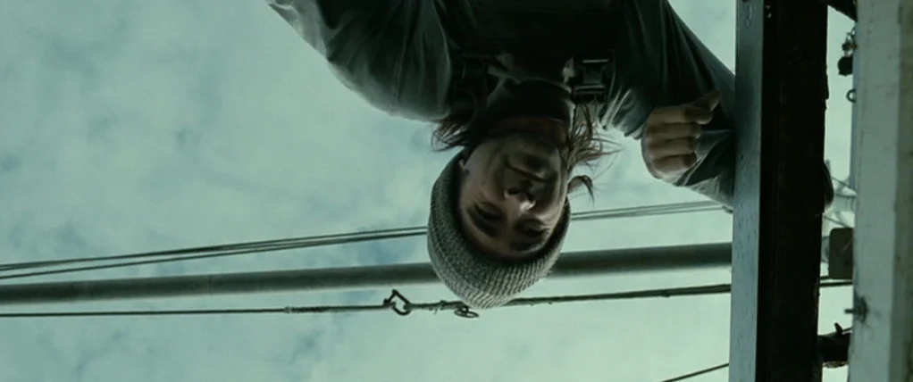 Ondine (2009) movie still: closeup — A view from beneath a structure looking up at a person on a boat. The subject wears a beanie and shirt while…