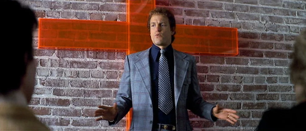 The People vs. Larry Flint (1996) movie still: medium — A man in a blazer stands in front of a brick wall displaying a cross. The man gestures with…