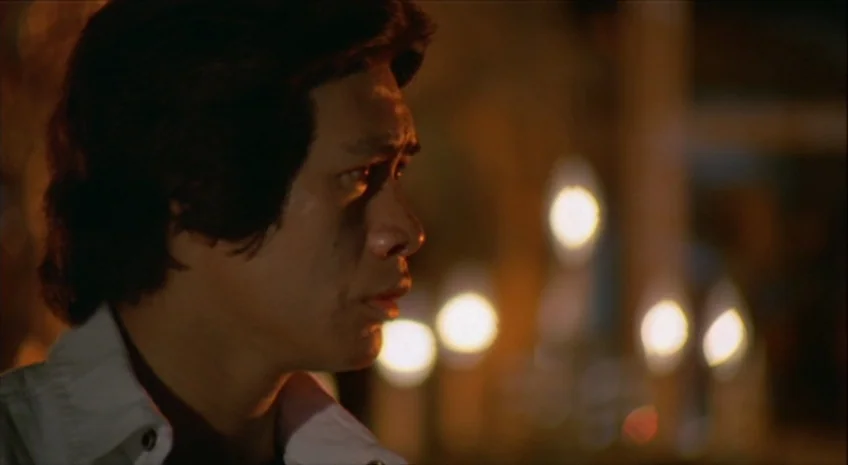 Boxer’s Omen (Mo) (1983) movie still: closeup — A dimly lit room features out-of-focus warm light sources in the background. A man turns his head to…