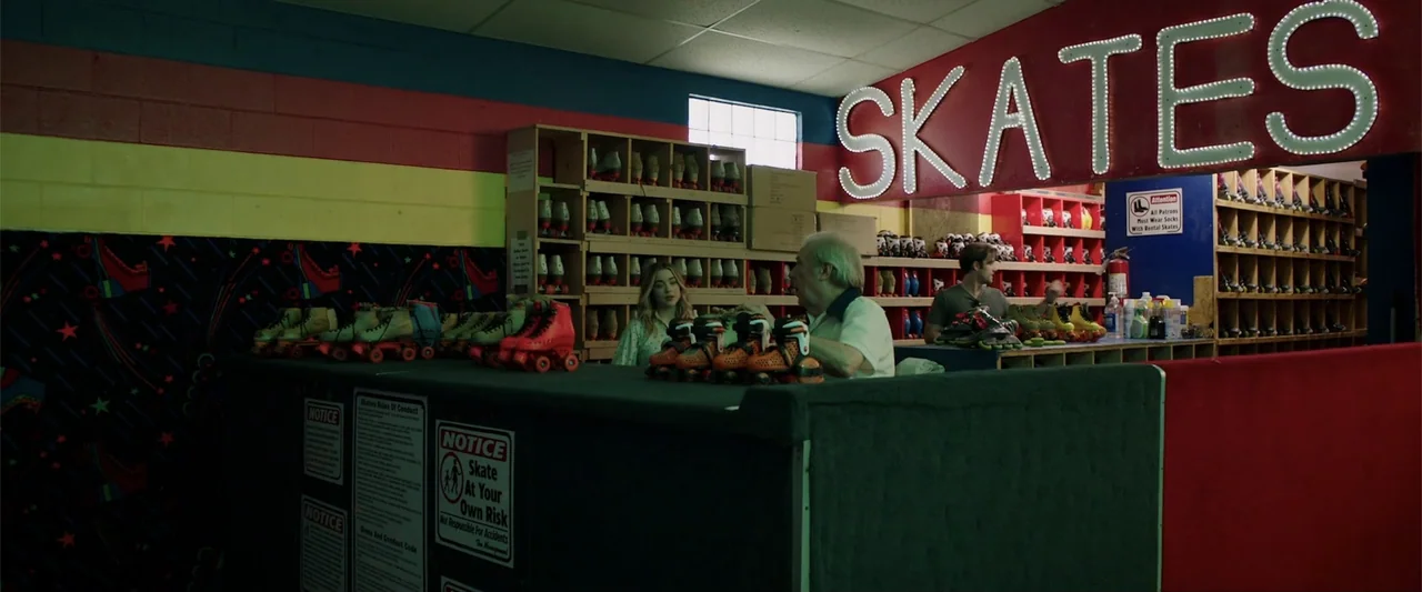 Playing God (2021) movie still: medium — A brightly lit skate rental counter features rows of rental skates on wooden shelves. A young woman speaks…