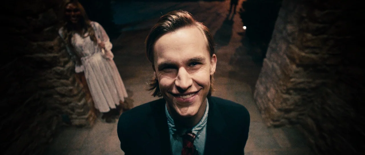 The Purge (2013) movie still: closeup — A stone-walled walkway at night with rough masonry sides and a paved floor. A smiling young man stands in…