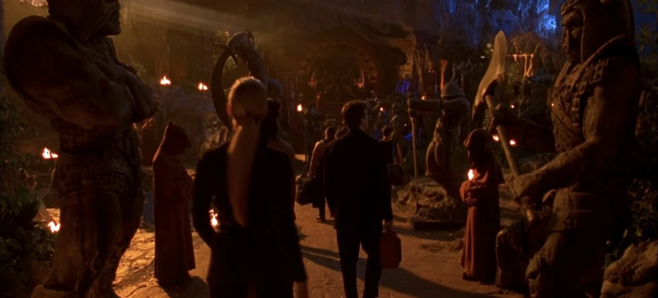 Mortal Kombat (2021) movie still: wide — A stone-walled underground chamber is lined with massive, archaic-looking warrior statues and torches. A…