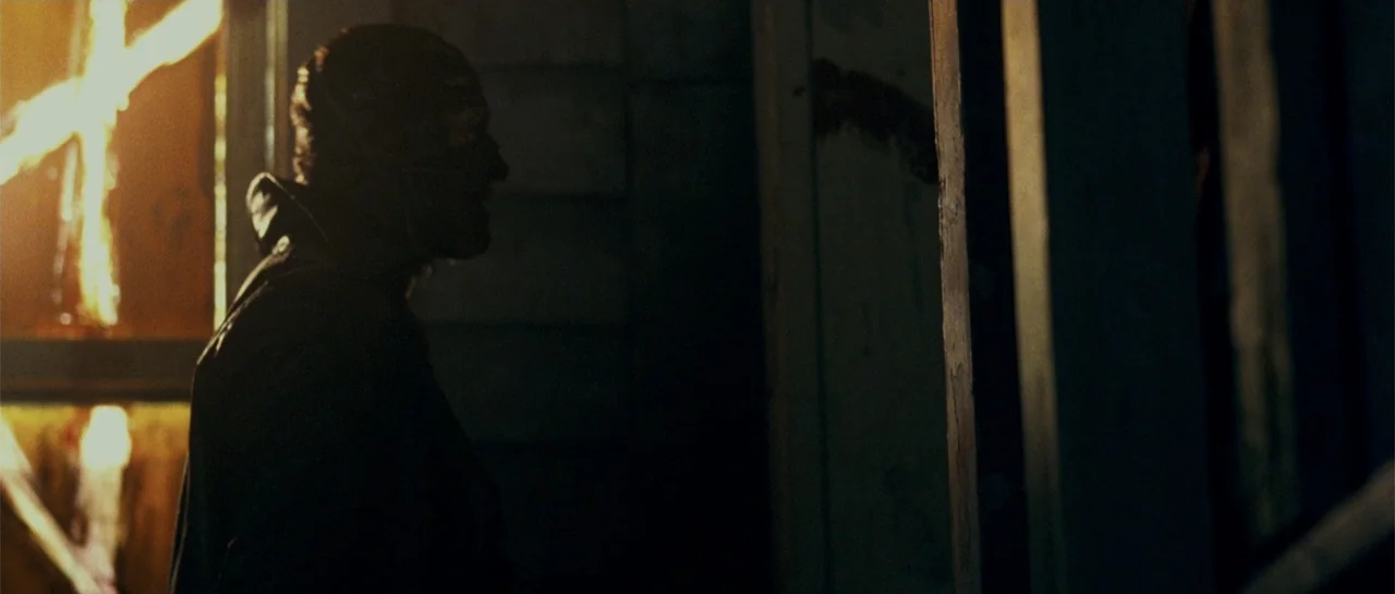 Blood Creek (2009) movie still: medium — A dimly lit space features a silhouetted man near a source of bright fire. The man stands in profile while…