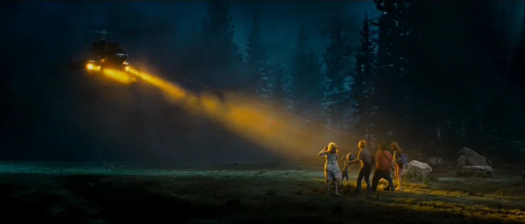 Paul (2011) movie still: wide — A dark, forested meadow at night is illuminated by a piercing helicopter searchlight. A small group of people stand…