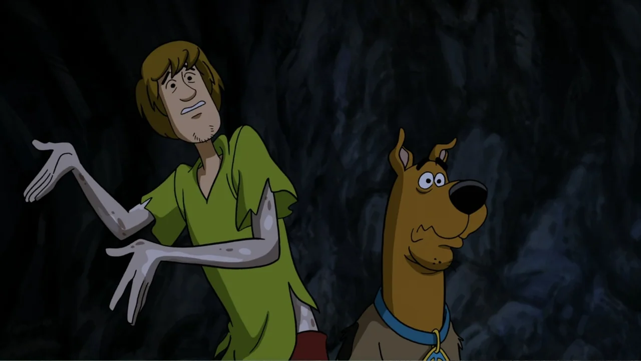 Scooby-Doo! Return to Zombie Island (2019) movie still: medium — A dark rocky cave interior with jagged textures lines the backdrop. A man in a…