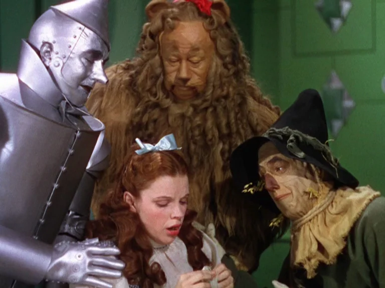 The Wizard Of Oz (1939) movie still: medium — A green-walled interior space where four costumed characters are clustered together. A young woman…