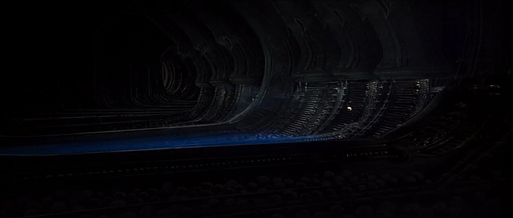 Alien (1979) movie still: establishing — A dark, curved alien structure features organic, ribbed walls receding into deep shadows. A thin horizontal…