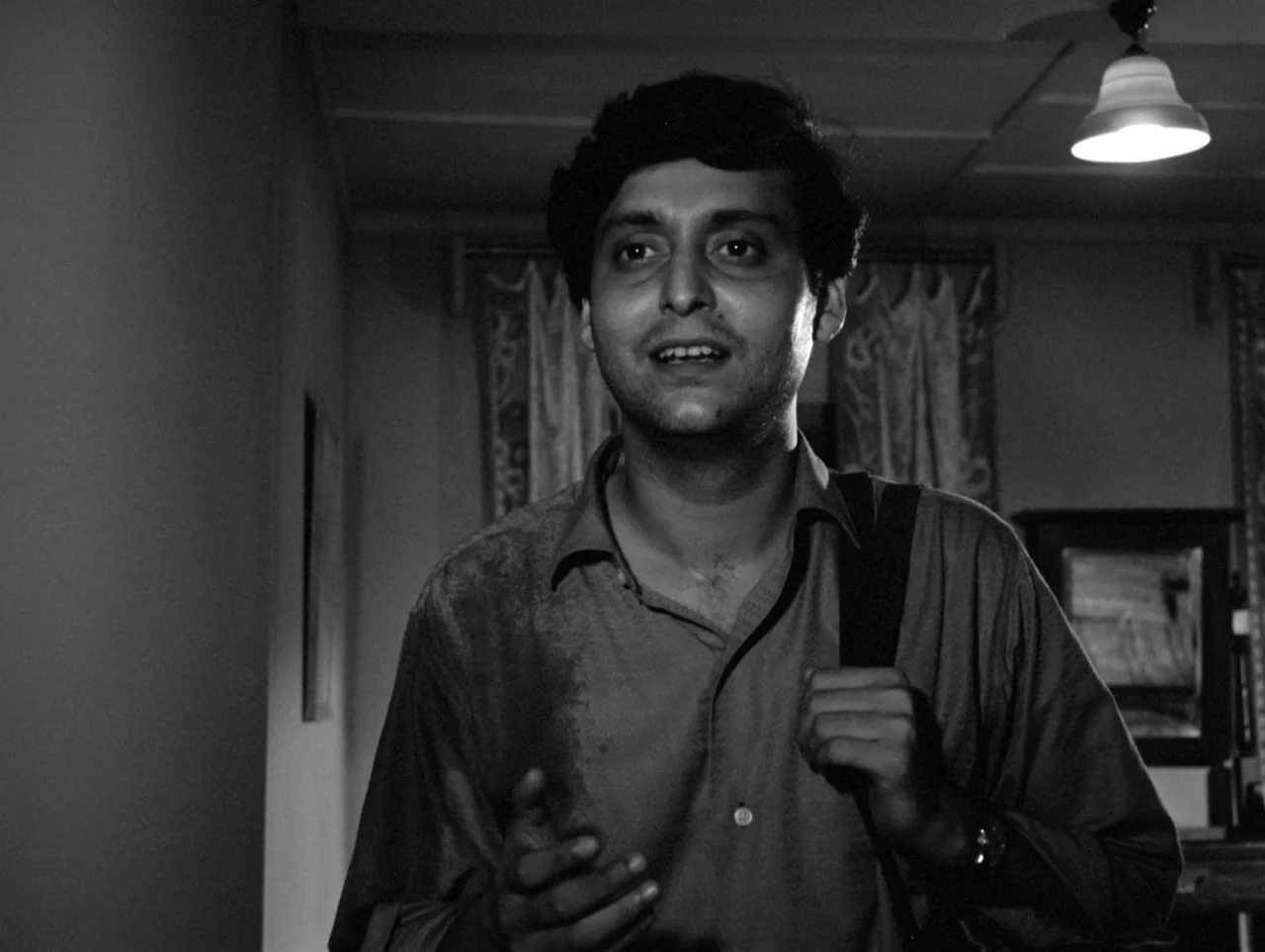 The Coward (1965) movie still: medium — An interior space with a curtained window and a hanging light fixture. A young man wearing a shirt stands in…