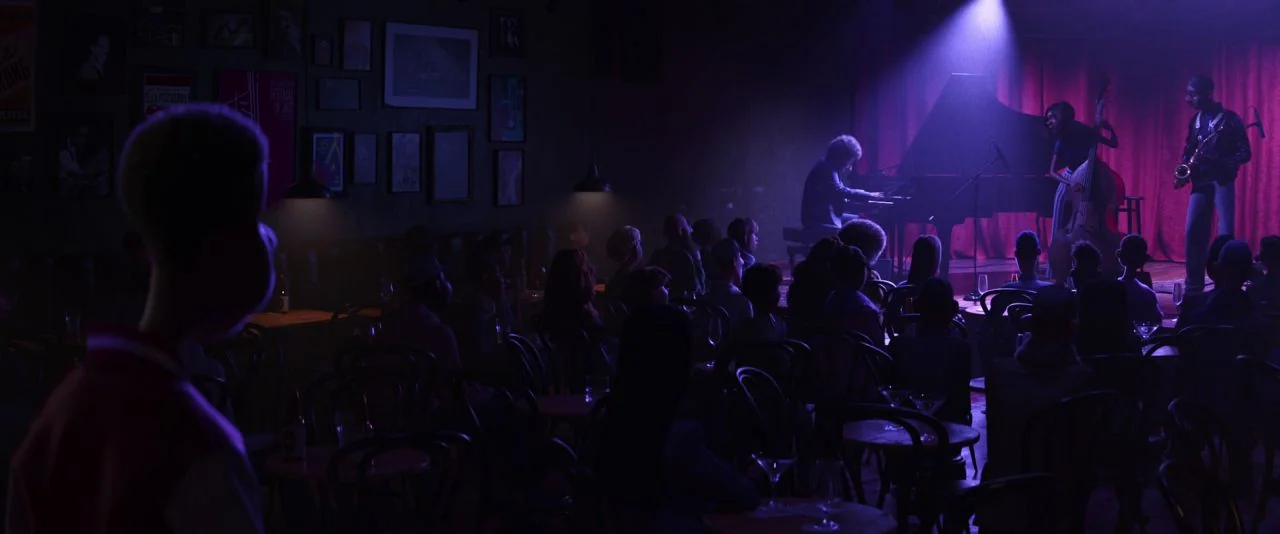 Soul (2020) movie still: wide — A dimly lit jazz club features a small stage with a performing musical quartet. Dark tables and chairs fill the…